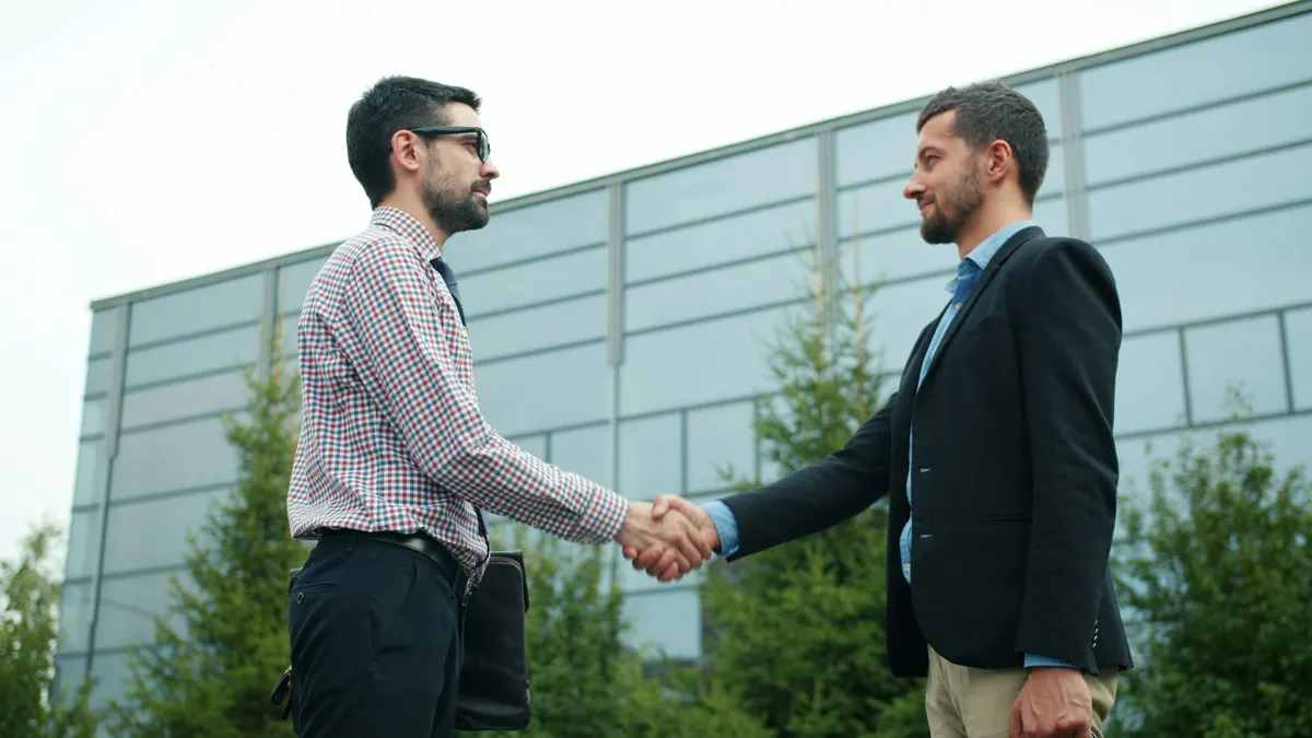 Deux hommes se serrant la main devant un bâtiment d'entreprise