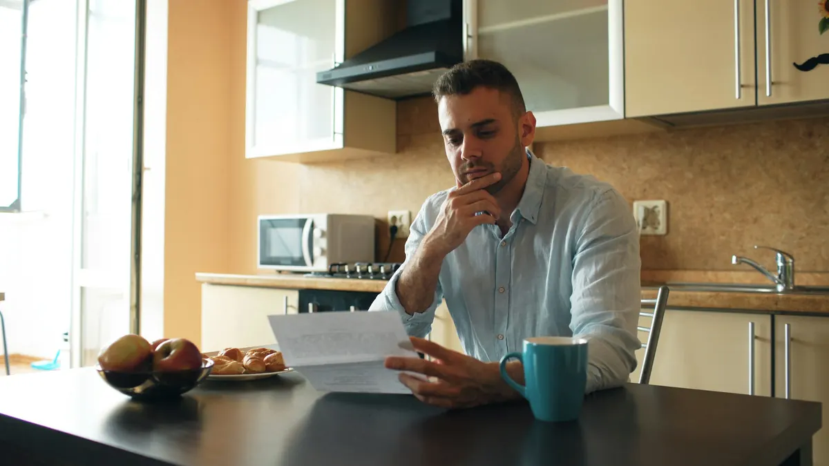 Homme pensif lisant un courrier à la table de sa cuisine