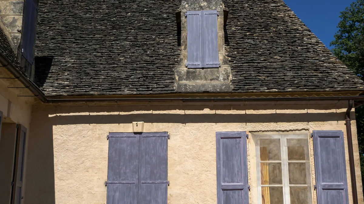 Façade d'une maison ancienne en pierre aux volets bleus