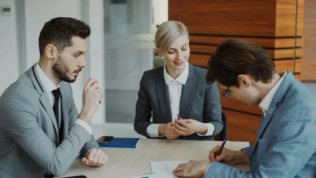 Réunion de travail à trois autour d'une table, l'un des participants signe un document