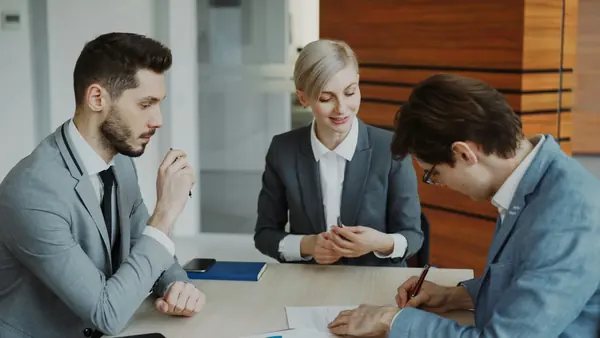 Réunion de travail à trois autour d'une table, l'un des participants signe un document